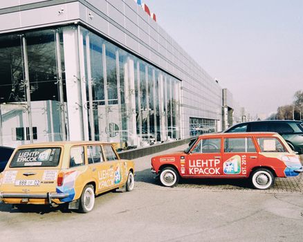 Vintage cars with vibrant paint in front of a modern glass building in Almaty, Kazakhstan.