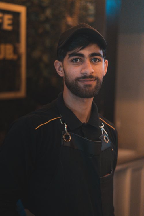 Free Portrait of a young male barista wearing a cap and apron in a coffee shop setting. Stock Photo