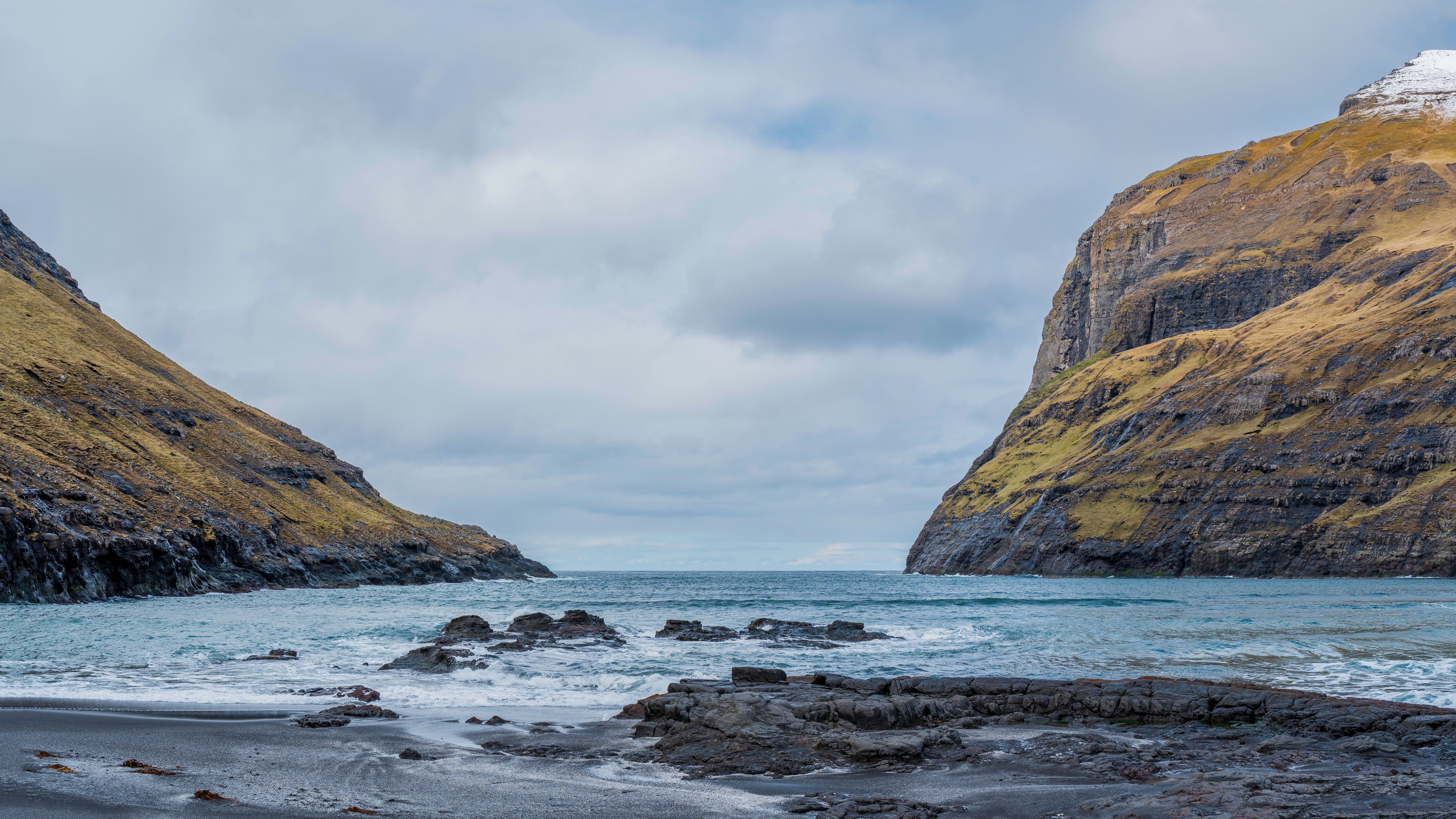Stunning coastal landscape with mossy cliffs and a wild beach under a cloudy sky in the Faroe Islands.