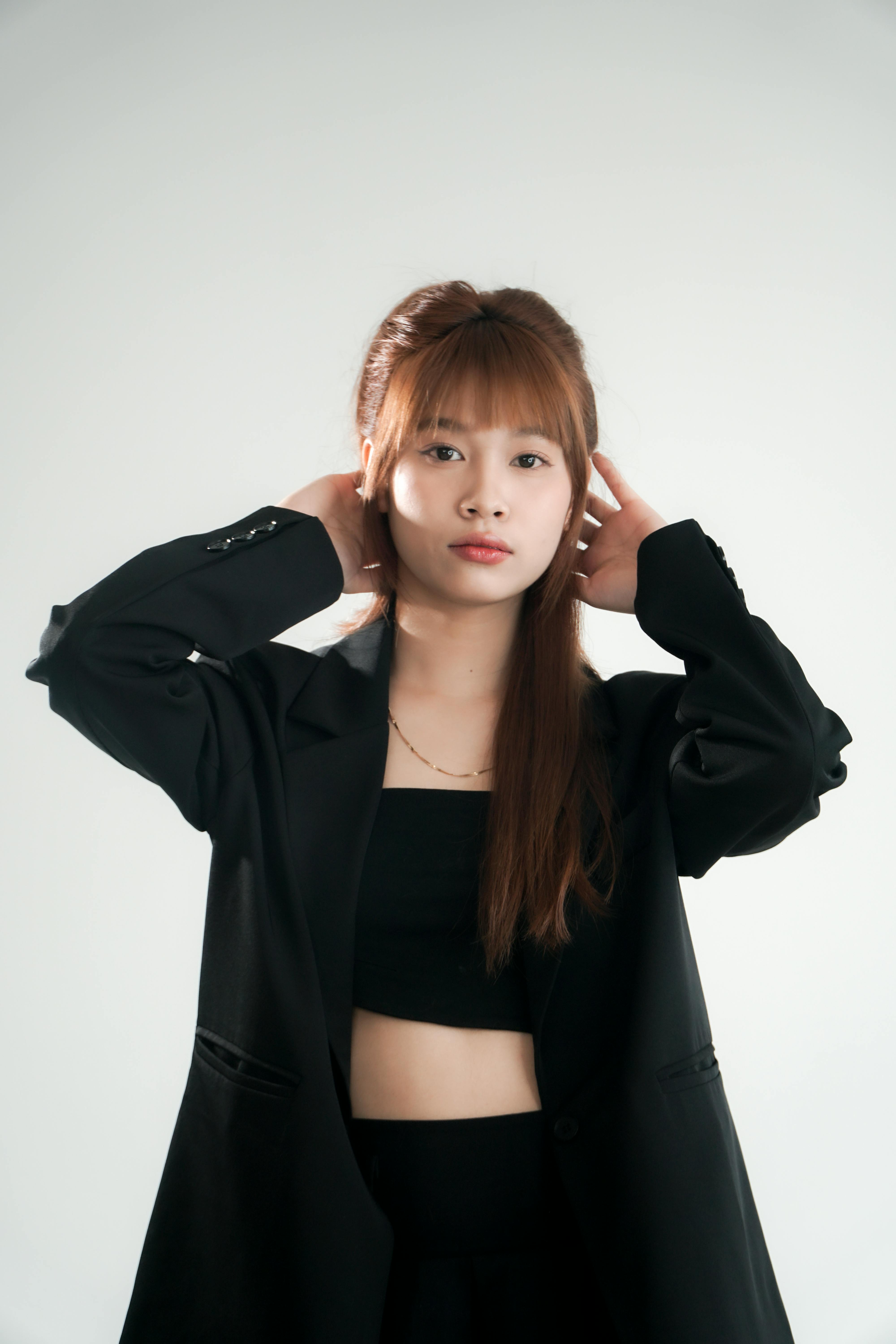 Portrait of a young woman wearing a black outfit, posing with hands on head.
