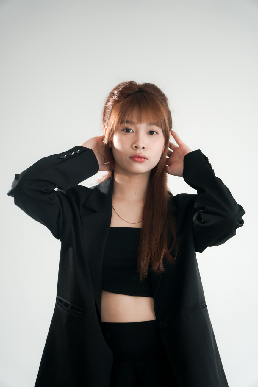Portrait of a young woman wearing a black outfit, posing with hands on head.