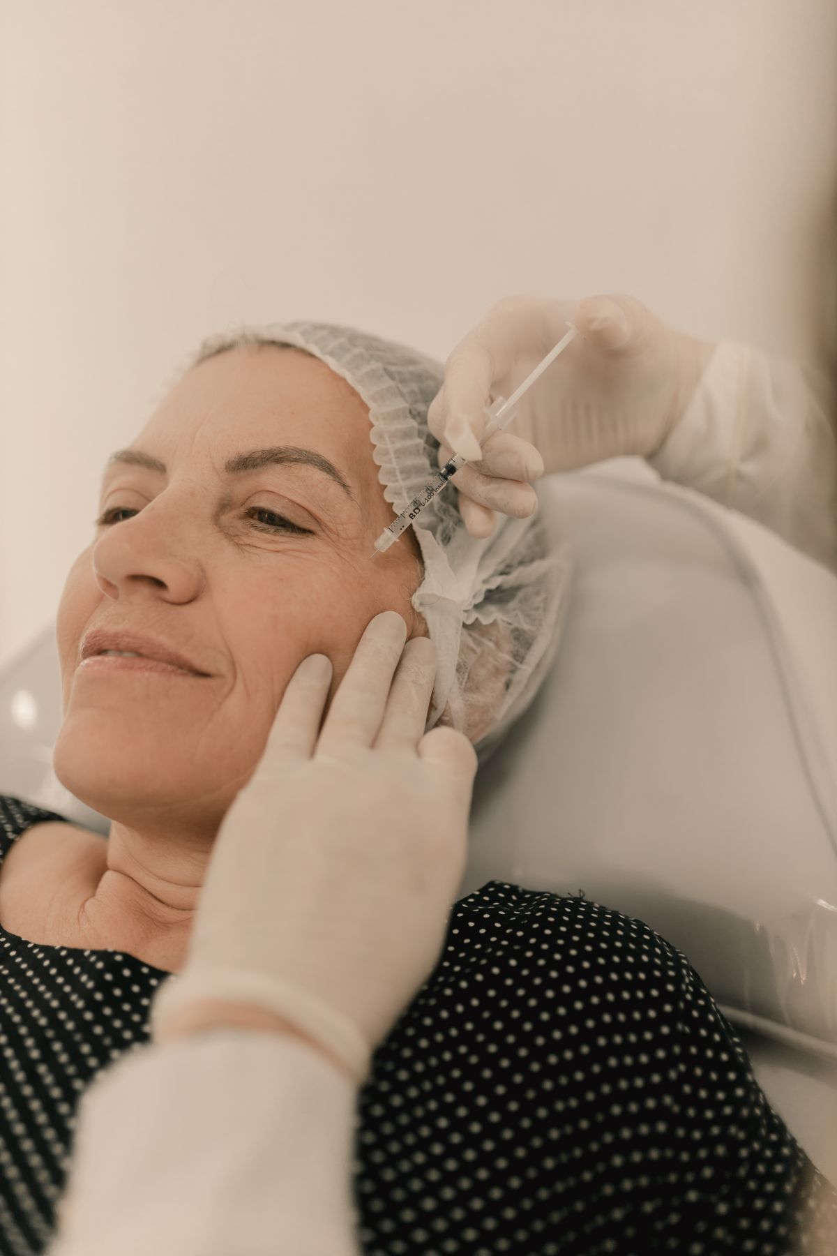 A middle-aged woman receiving a small cosmetic injection to the upper face from a gloved provider, representing newer wrinkle relaxers such as Jeuveau, Xeomin and DAXXIFY offered in Virginia Beach