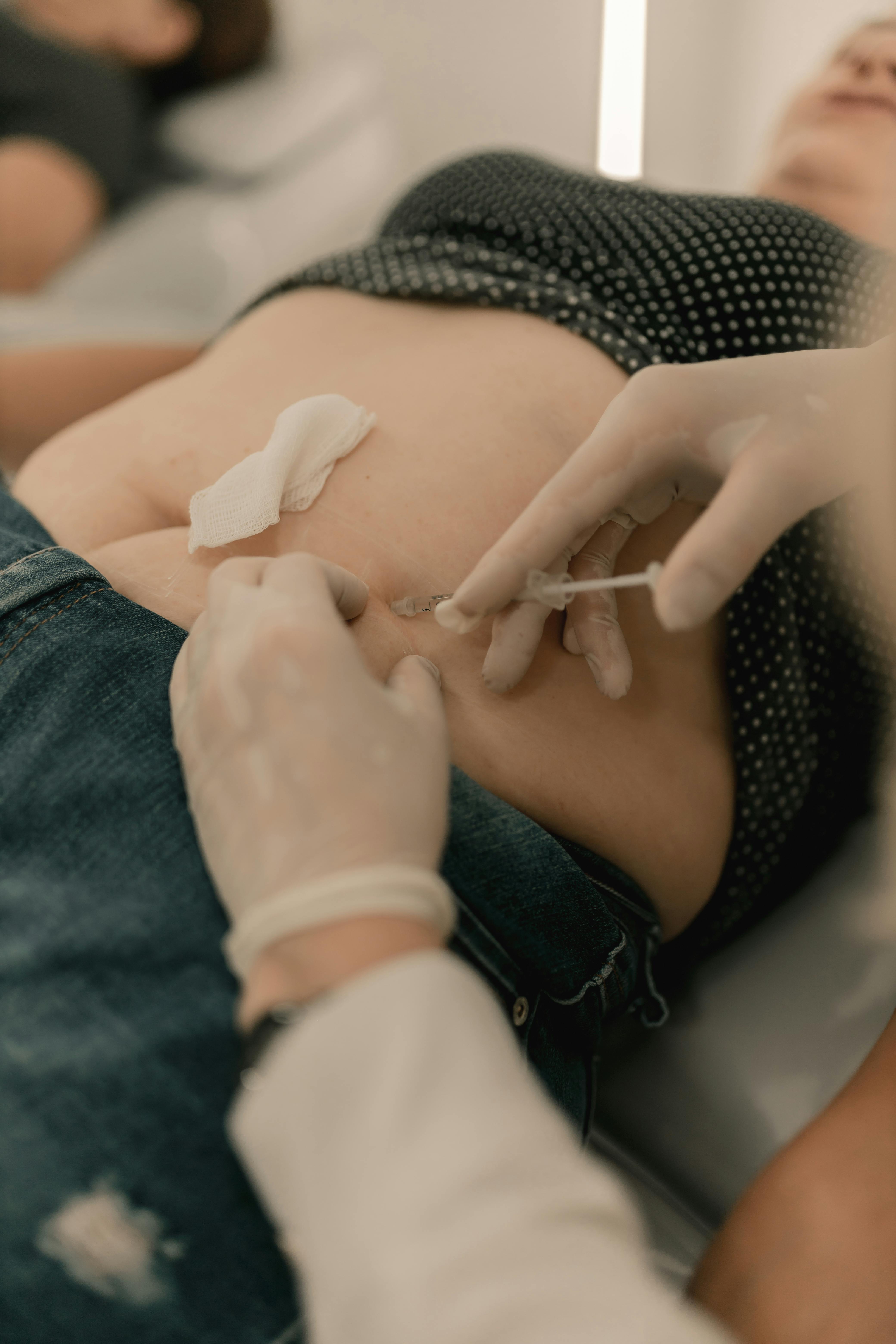 A close-up view of a medical professional performing a stomach injection.