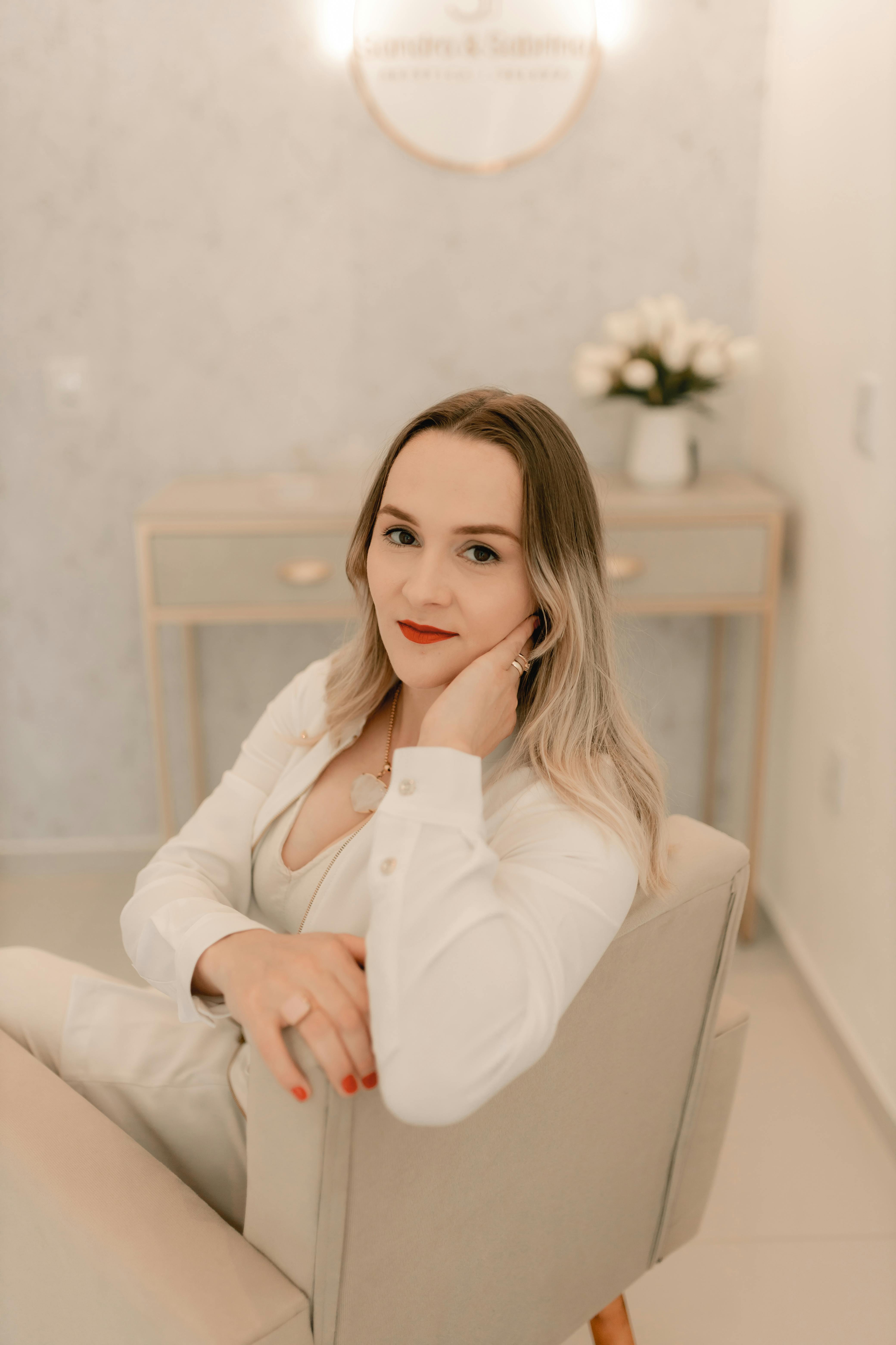 Stylish woman sitting in a modern, minimalist interior space with neutral tones.