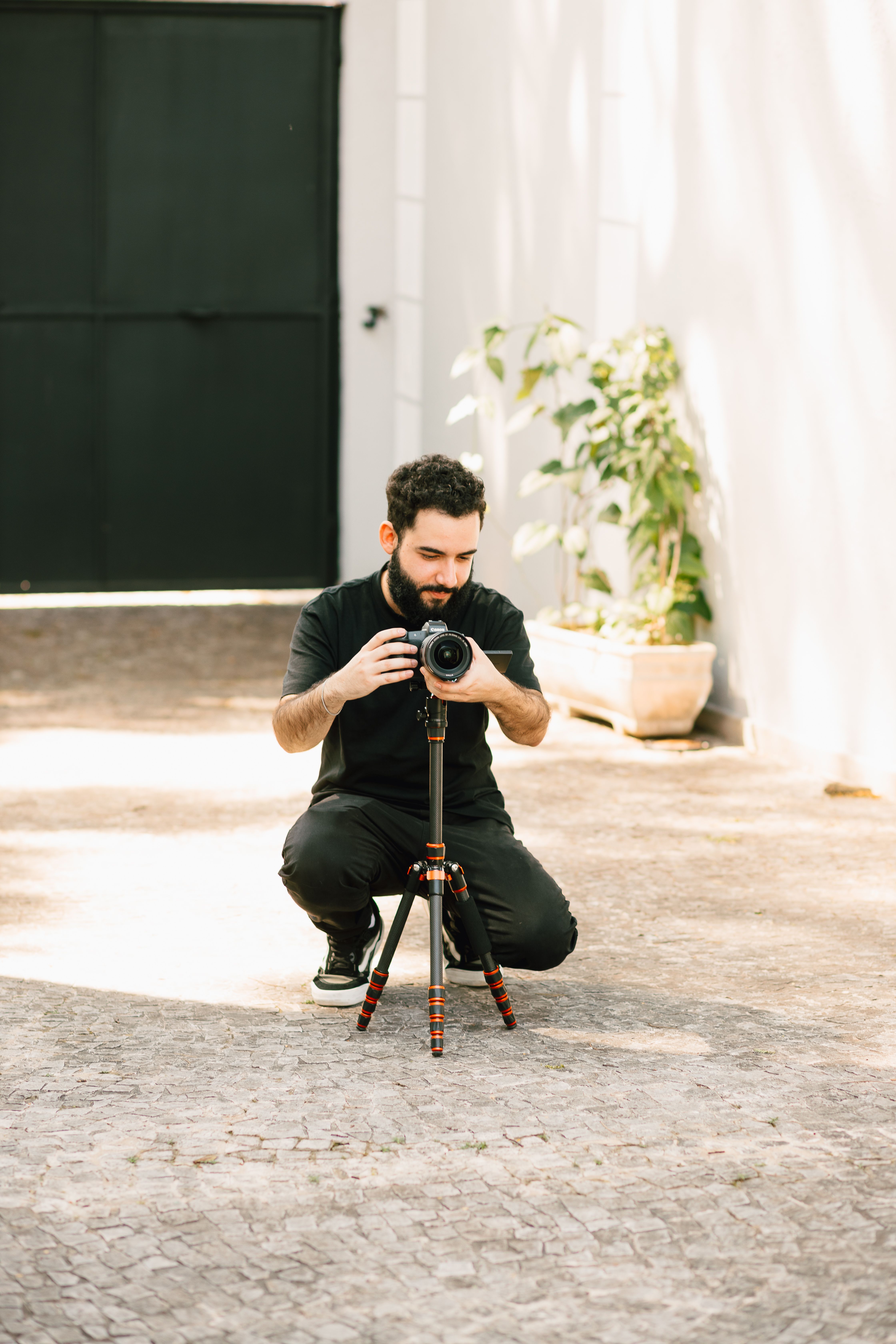 A photographer kneels while adjusting a camera on a tripod in an outdoor setting.
