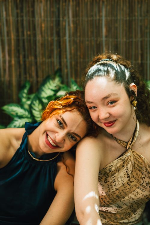 Free Two women smiling while seated outdoors, enjoying a sunny day. Stock Photo