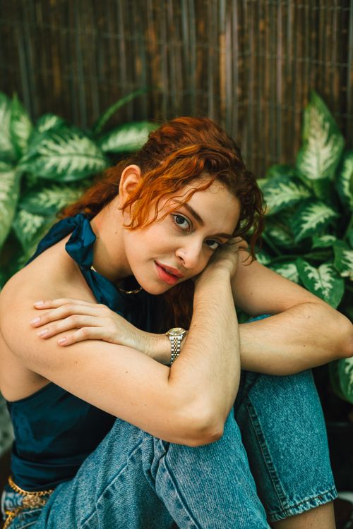 Free Casual portrait of a woman with curly hair in a relaxed setting surrounded by greenery. Stock Photo