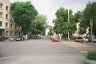 城市街景中，汽车停放在路边，行人正使用人行横道，道路两旁排列着树木