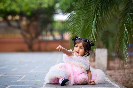 Adorable baby girl enjoying a playful moment outdoors in a pink dress with green scenery.