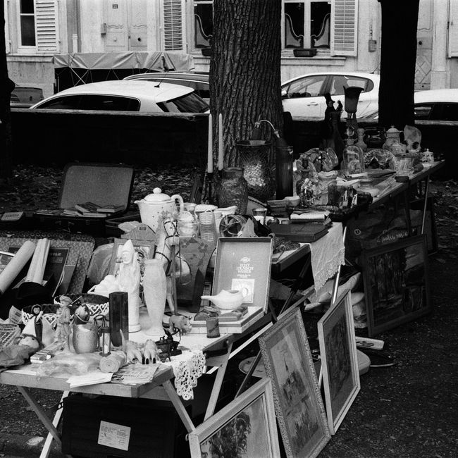 Black and white image of a vintage flea market in Nancy, France with eclectic items.