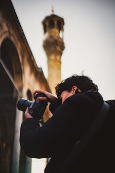 A person photographing historical architecture under a tall tower outdoors.