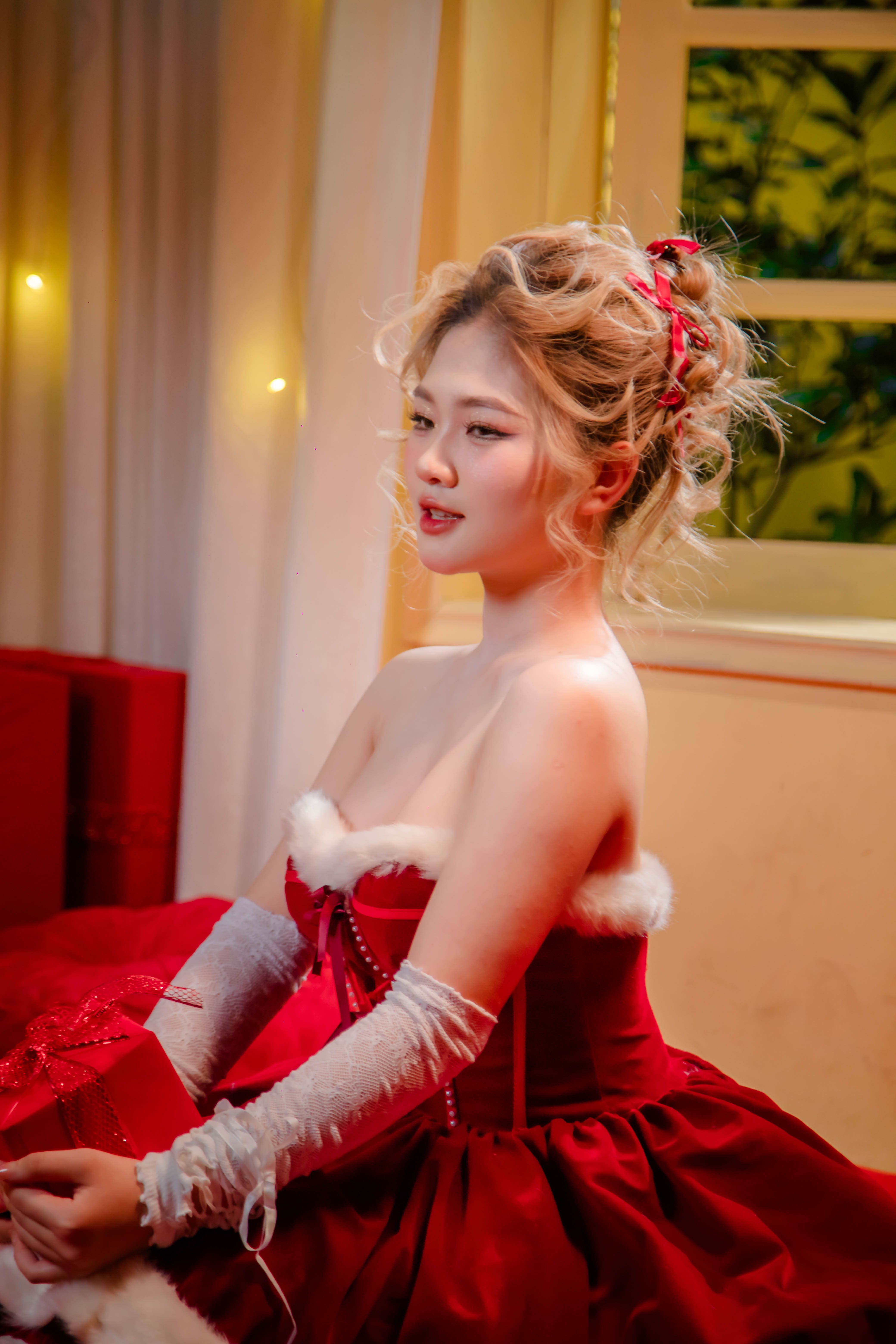 Elegant woman in red dress with festive decor enjoying a cozy indoor setting.