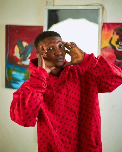 Free A young man making a playful expression while wearing a red hoodie, indoor setting with colorful art in the background. Stock Photo