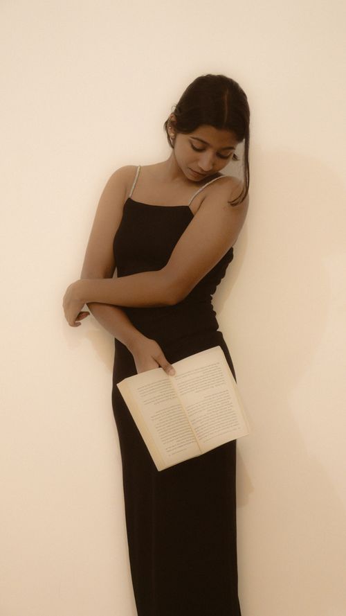 Free Young woman in a black dress reads a book against a neutral background, exuding elegance. Stock Photo