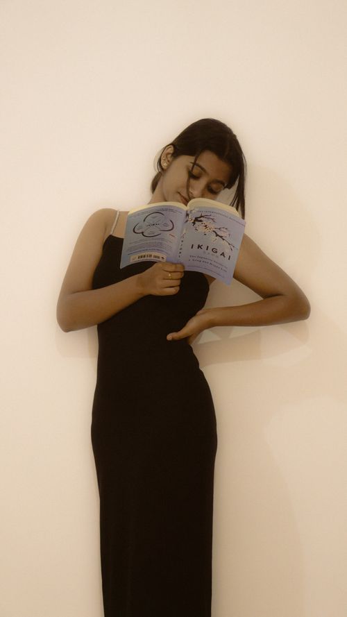 Free A thoughtful portrait of a young woman in a black dress reading Ikigai indoors. Stock Photo