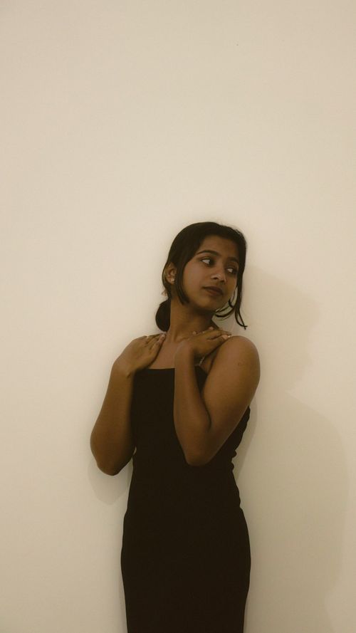 Free Portrait of a stylish young woman in a black dress, posing against a minimalist white background. Stock Photo