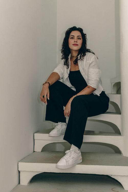 Free Confident woman in casual attire sits gracefully on a white staircase indoors. Stock Photo