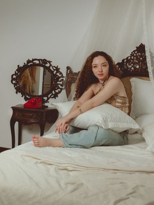 Free Young woman relaxing on a bed in a stylish vintage-themed room with ornamental mirror and retro phone. Stock Photo