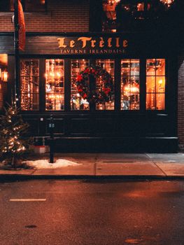 Warmly lit Irish tavern exterior decorated for the holidays at night, showcasing a welcoming festive atmosphere.