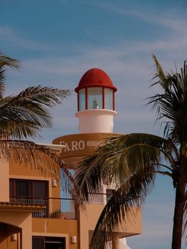 A vibrant lighthouse surrounded by palm trees under a clear blue sky.