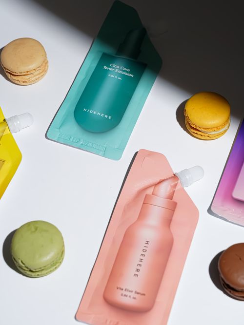 Free Vibrant skincare sachets paired with colorful macarons on a flat lay, perfect for lifestyle imagery. Stock Photo