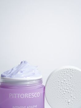 Close-up of an open jar of purple azulene cream with water droplets on the lid.