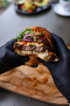 Close-up of a gourmet burger with fresh ingredients held in black gloves, perfect for food lovers.