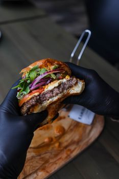 Close-up of a delicious beef burger with fresh veggies held by hands.