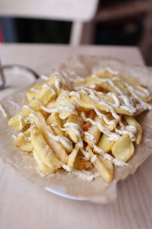 Free Crispy French fries drizzled with creamy sauce on a parchment-lined plate. Stock Photo