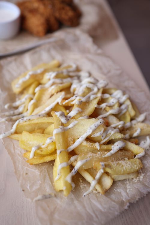 Free Delicious crispy french fries drizzled with creamy white sauce on parchment paper. Stock Photo