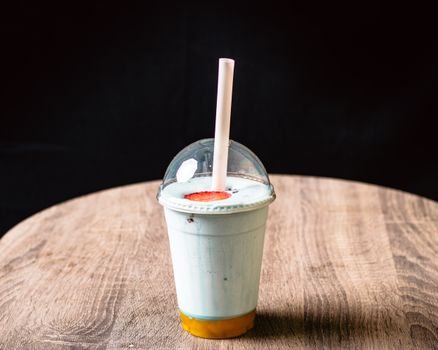 A blue milkshake in a plastic cup with dome lid and straw on a wooden table.