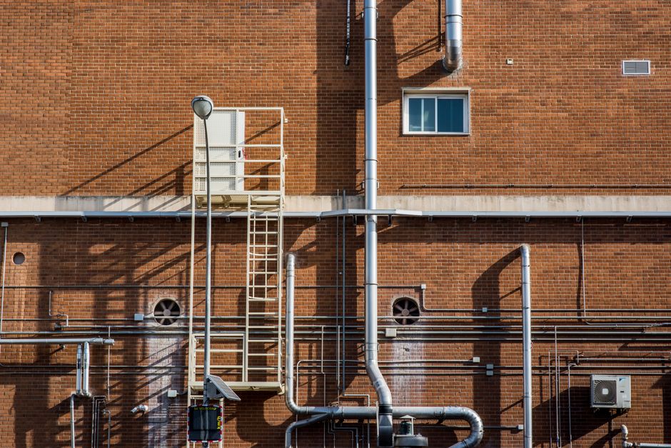 Detailed image of a brick wall with industrial piping and a ladder.