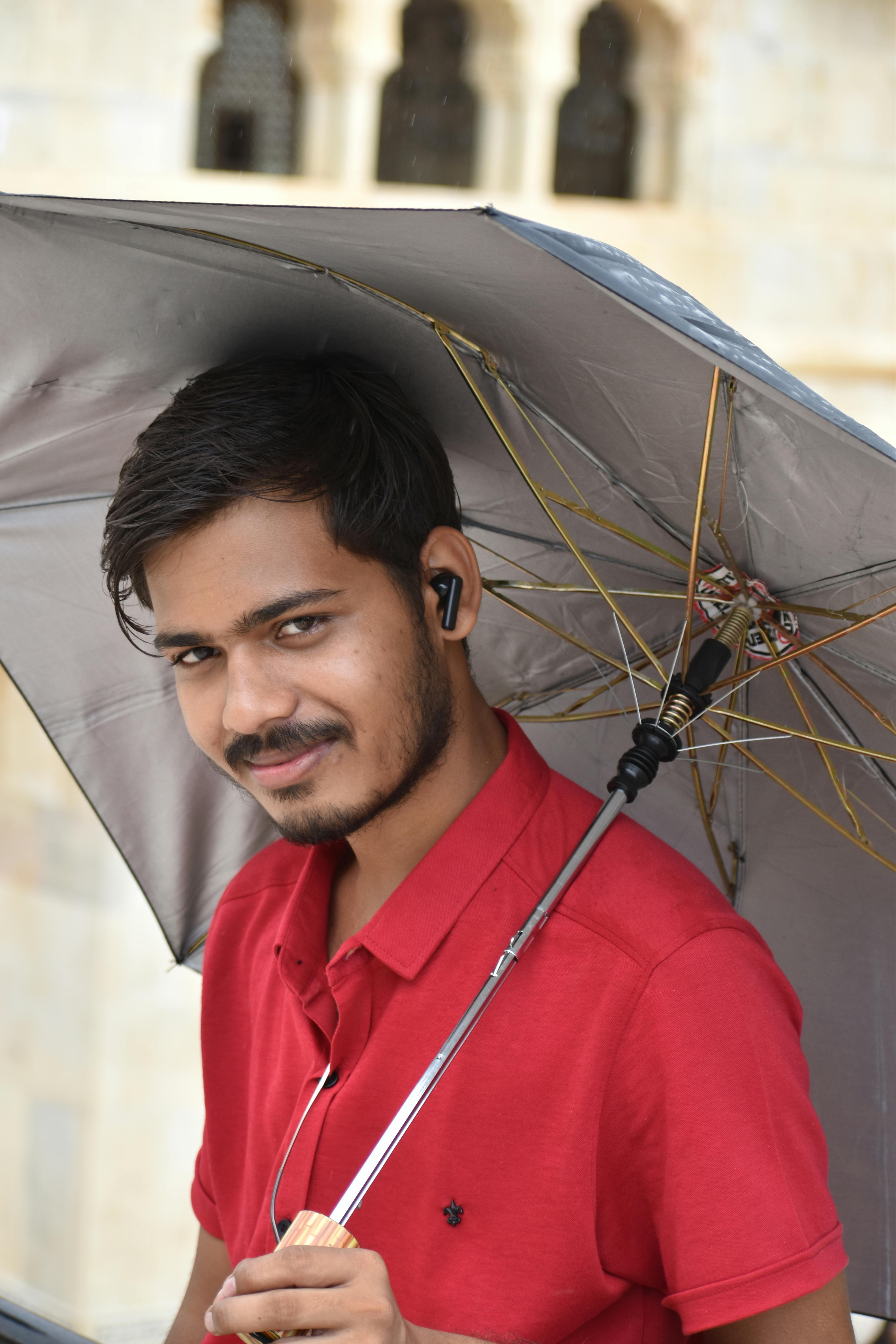 Smiling young man holding an umbrella, posing outdoors on a rainy day.