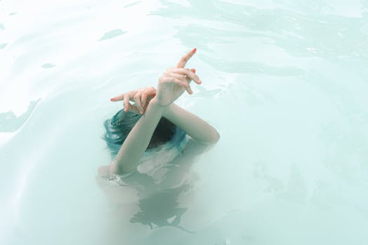 这是一张水下艺术镜头，拍摄了淹没在水中的一个人，其双手优雅地伸出水面