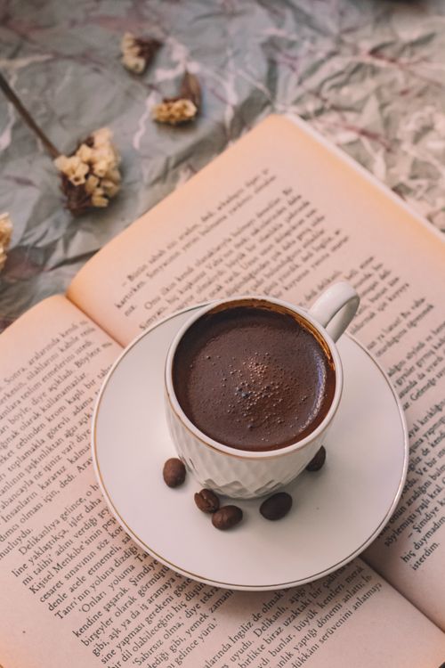 Free A warm cup of coffee sits atop an open book, surrounded by coffee beans, creating a cozy atmosphere. Stock Photo