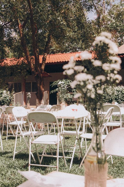 Montaje de evento en jardín soleado con sillas blancas y arreglos florales