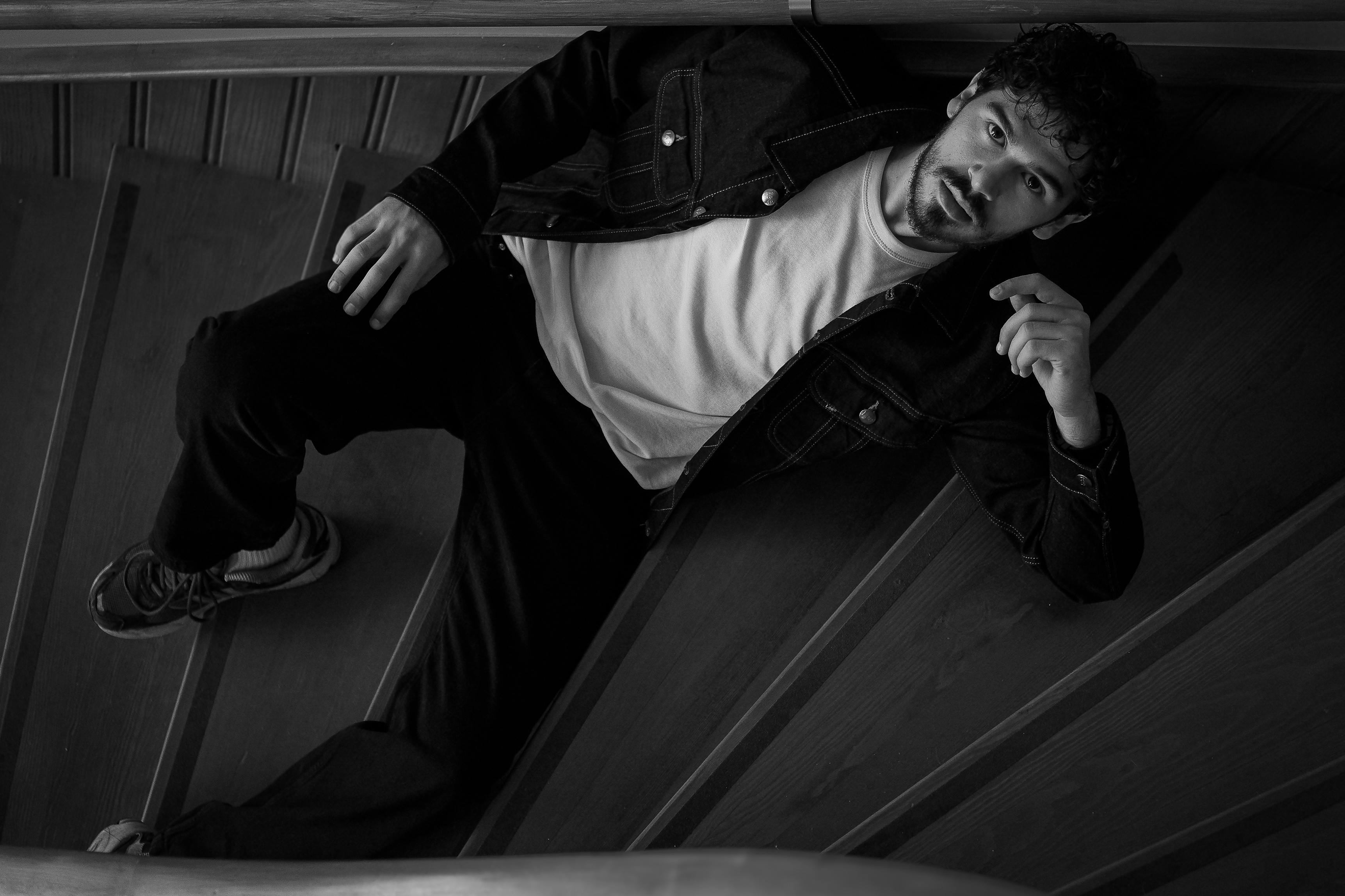 Black and white photo of a man reclining on wooden stairs, creating a moody and introspective vibe.