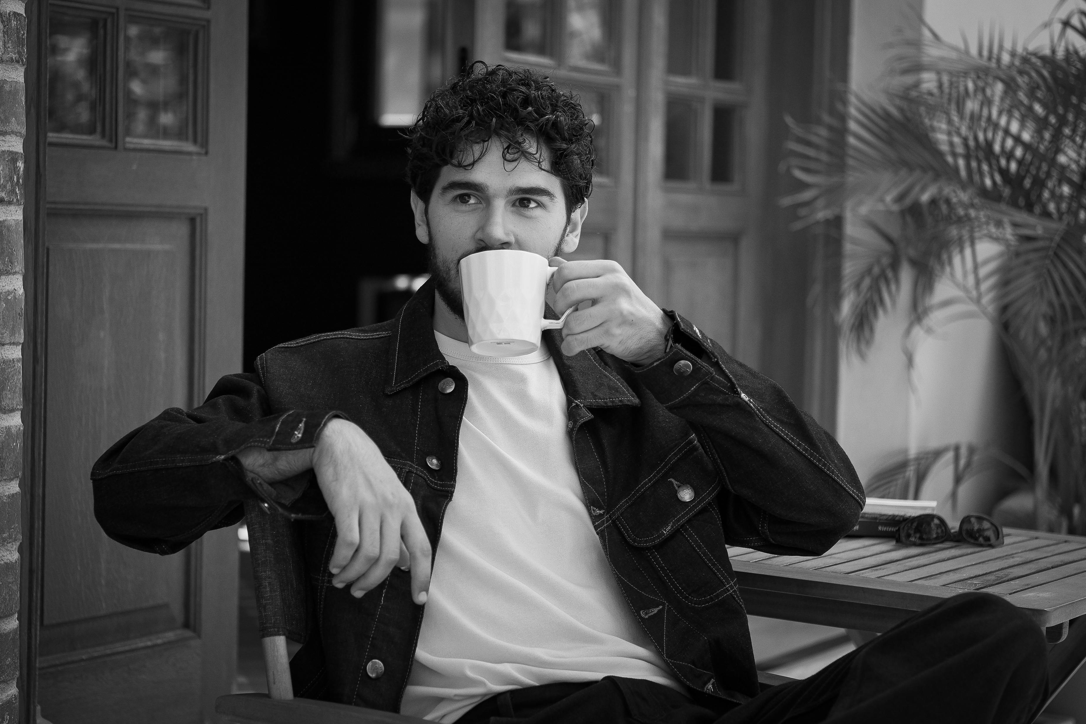 Relaxed black and white portrait of a man enjoying coffee outdoors.