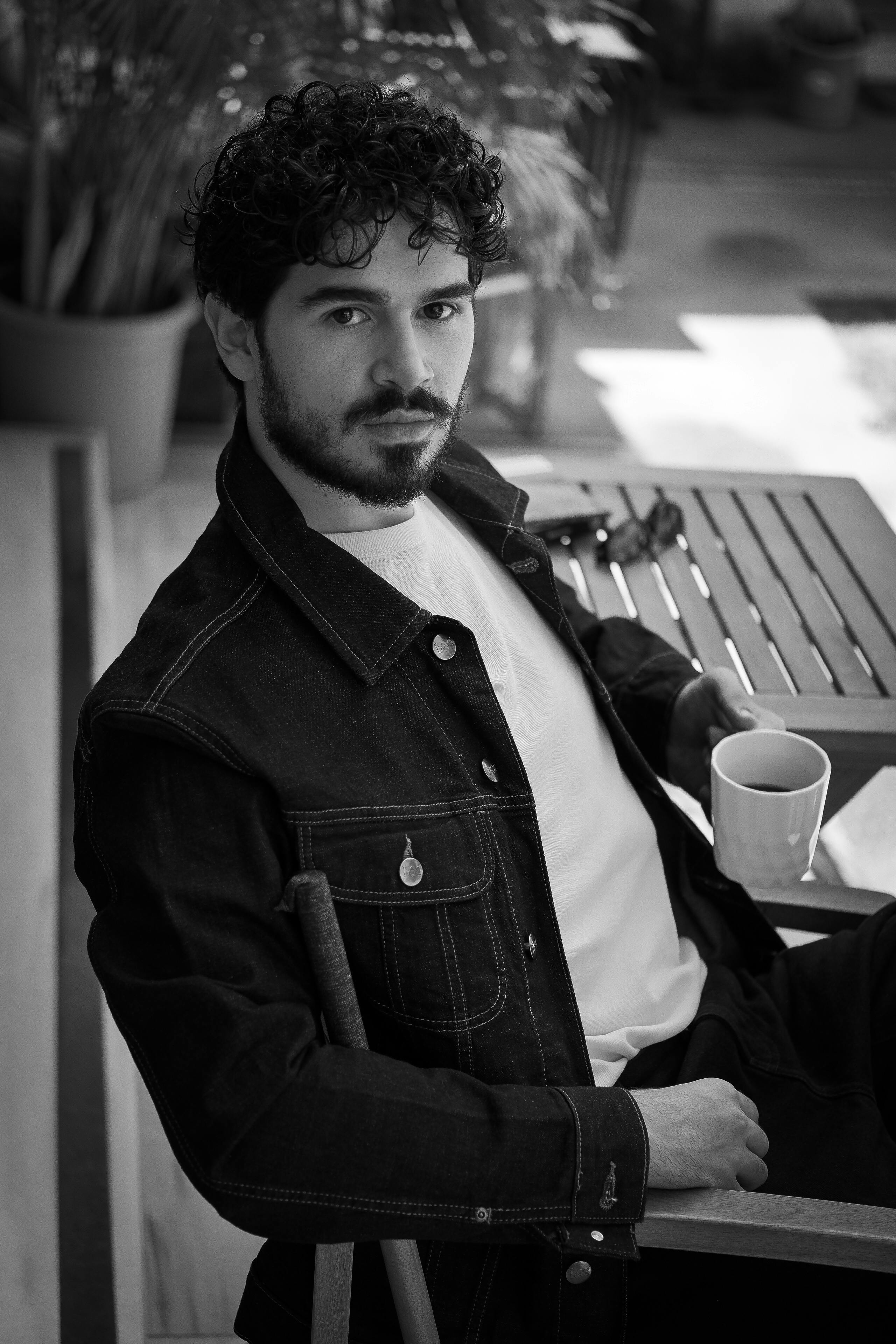 Black and white portrait of a stylish man holding a cup of coffee indoors.