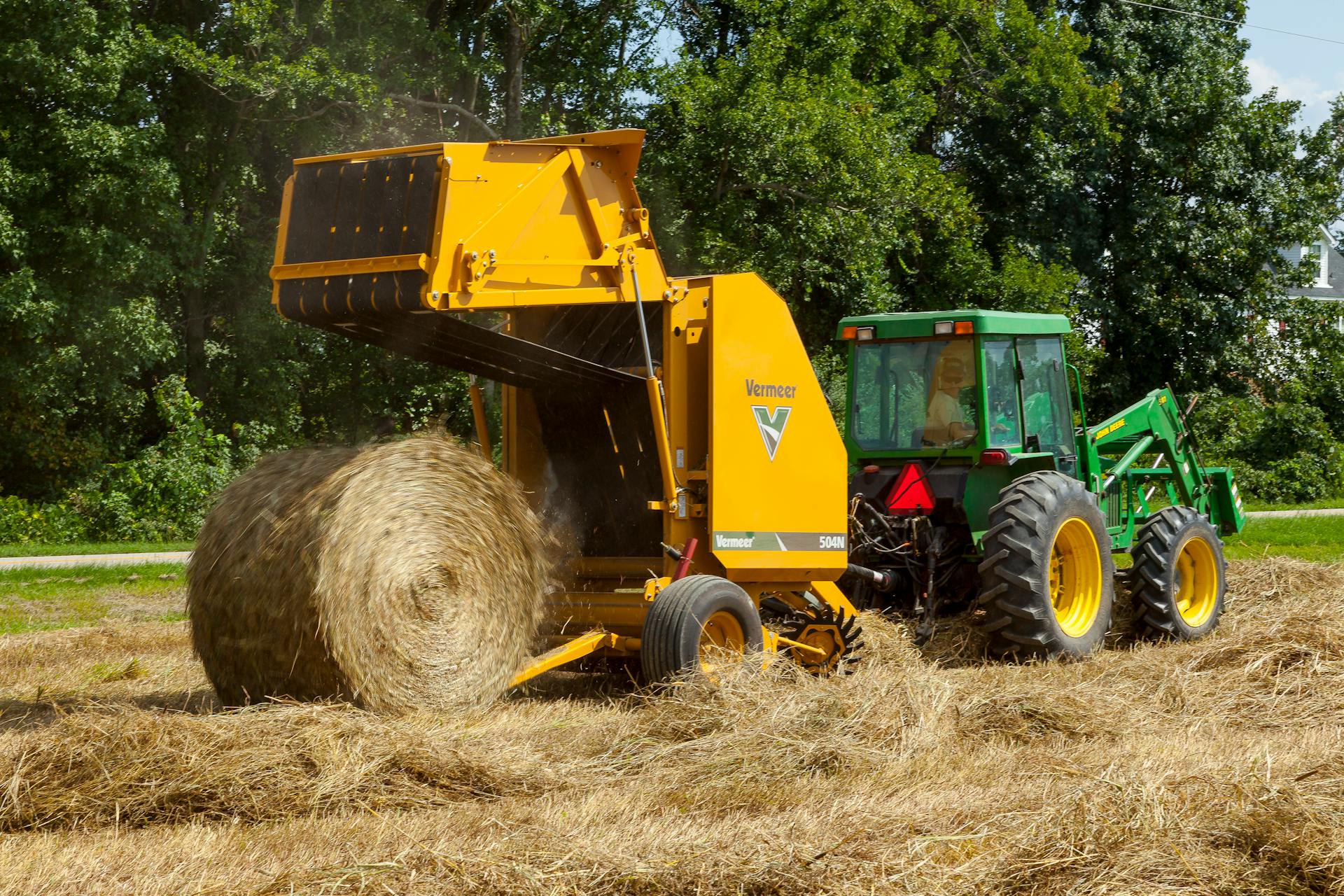 A tractor and baler machine working together to form a hay bale in a sunny field.