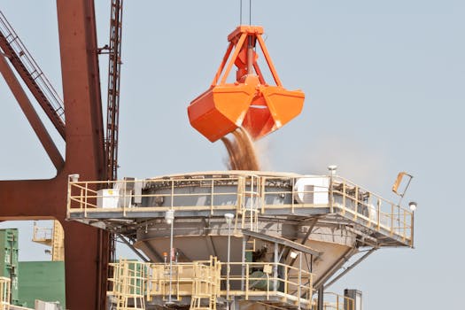 An industrial clamshell bucket unloading bulk materials at a port facility.