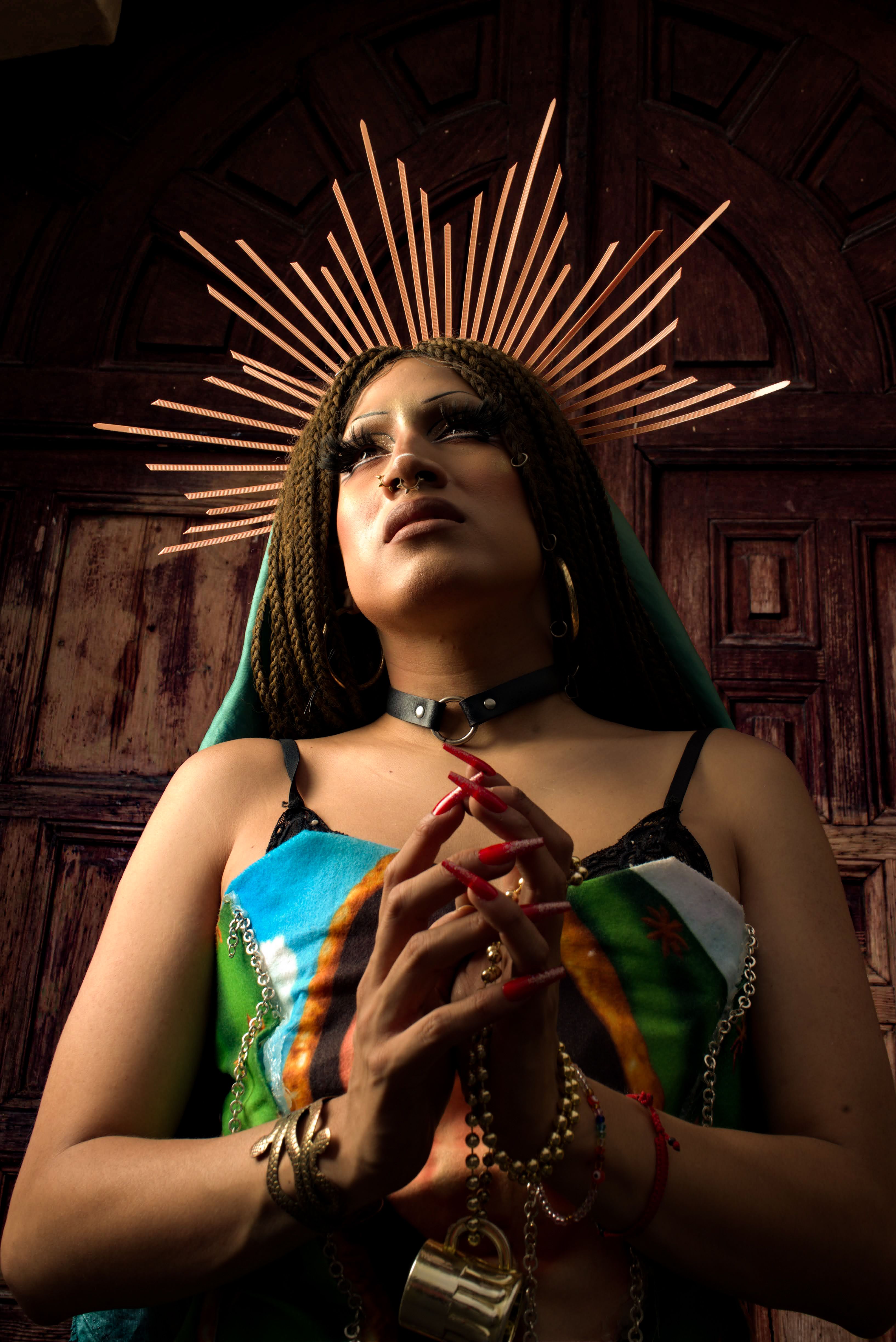 A powerful portrait of a person posing with a halo-like headdress in a prayerful stance, evoking religious and spiritual themes.