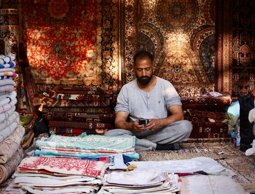 Free Middle-aged man in a carpet shop using phone amidst traditional textiles. Stock Photo