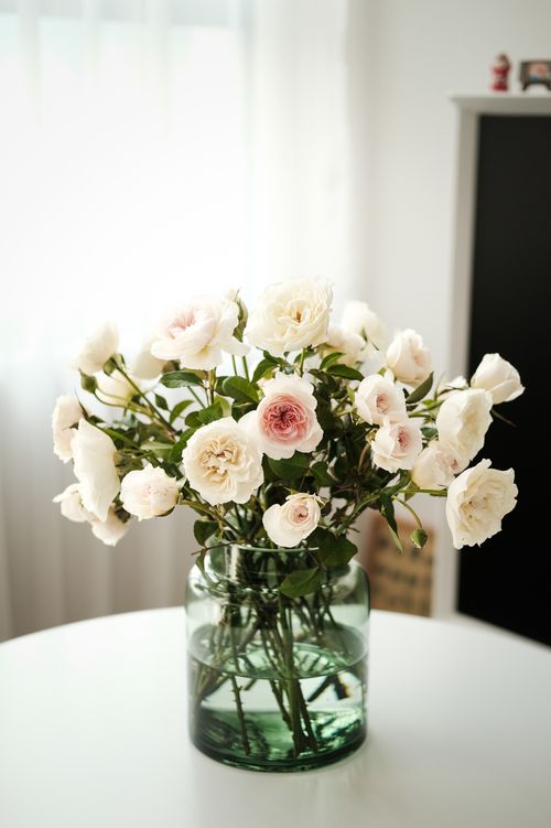 Free Beautiful white roses elegantly arranged in a clear glass vase, creating a serene and classic floral display. Stock Photo