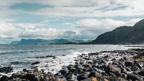 Free Explore the stunning rocky coastline of Norway with waves crashing and mountains in the distance under a cloudy sky. Stock Photo