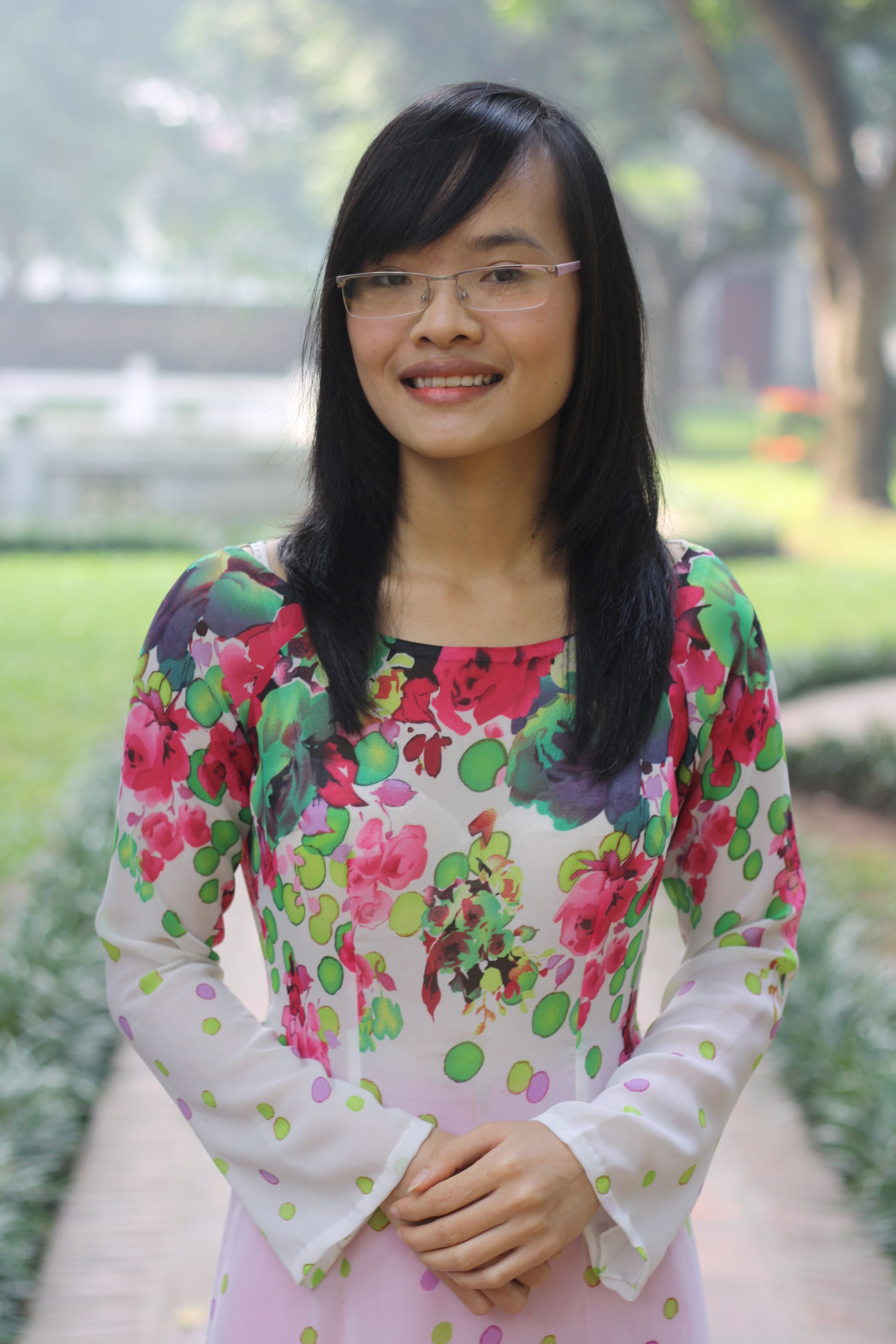 Woman in floral traditional dress smiling outdoors on a sunny day.