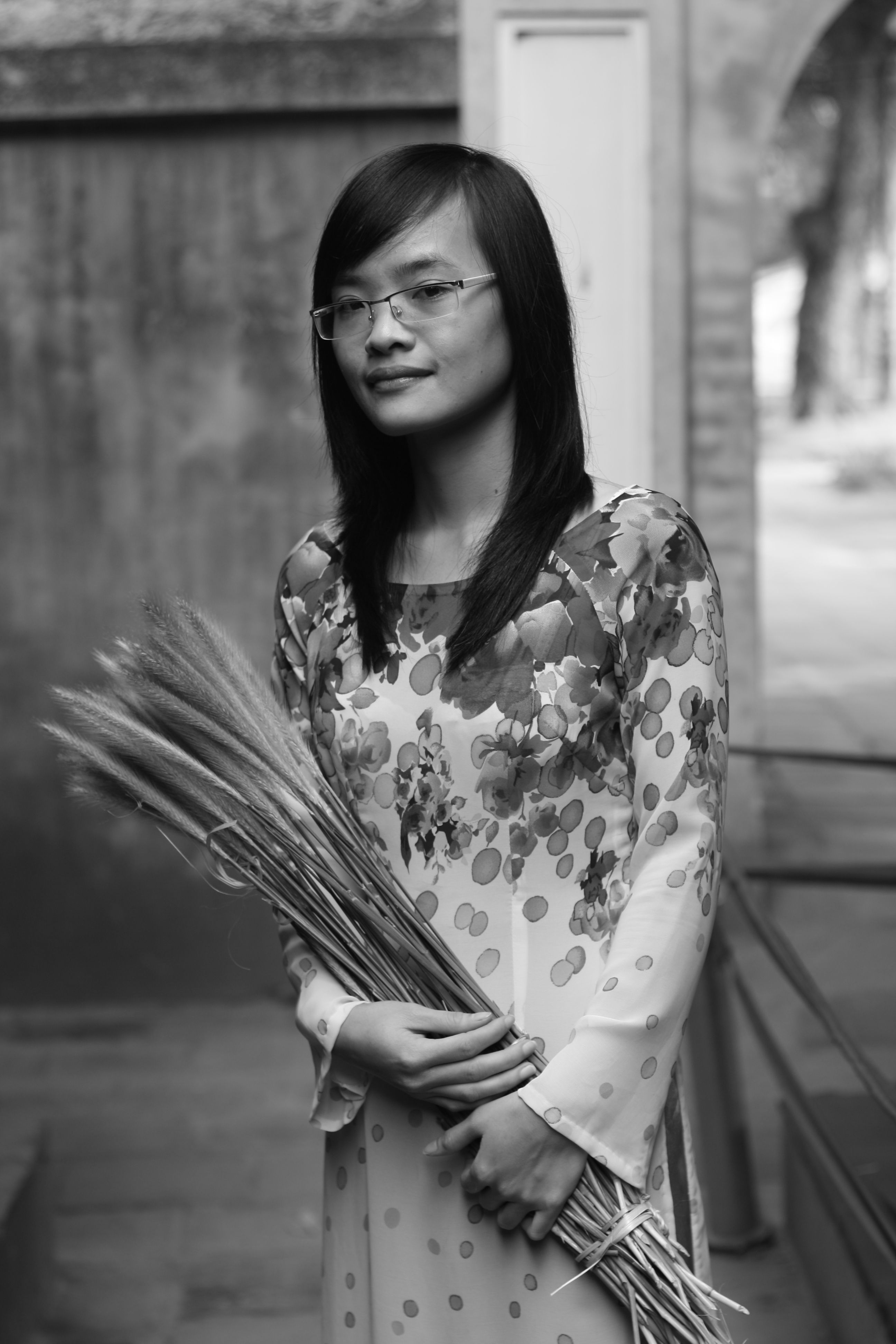 Elegant woman in a floral dress holding wheat in a grayscale portrait.