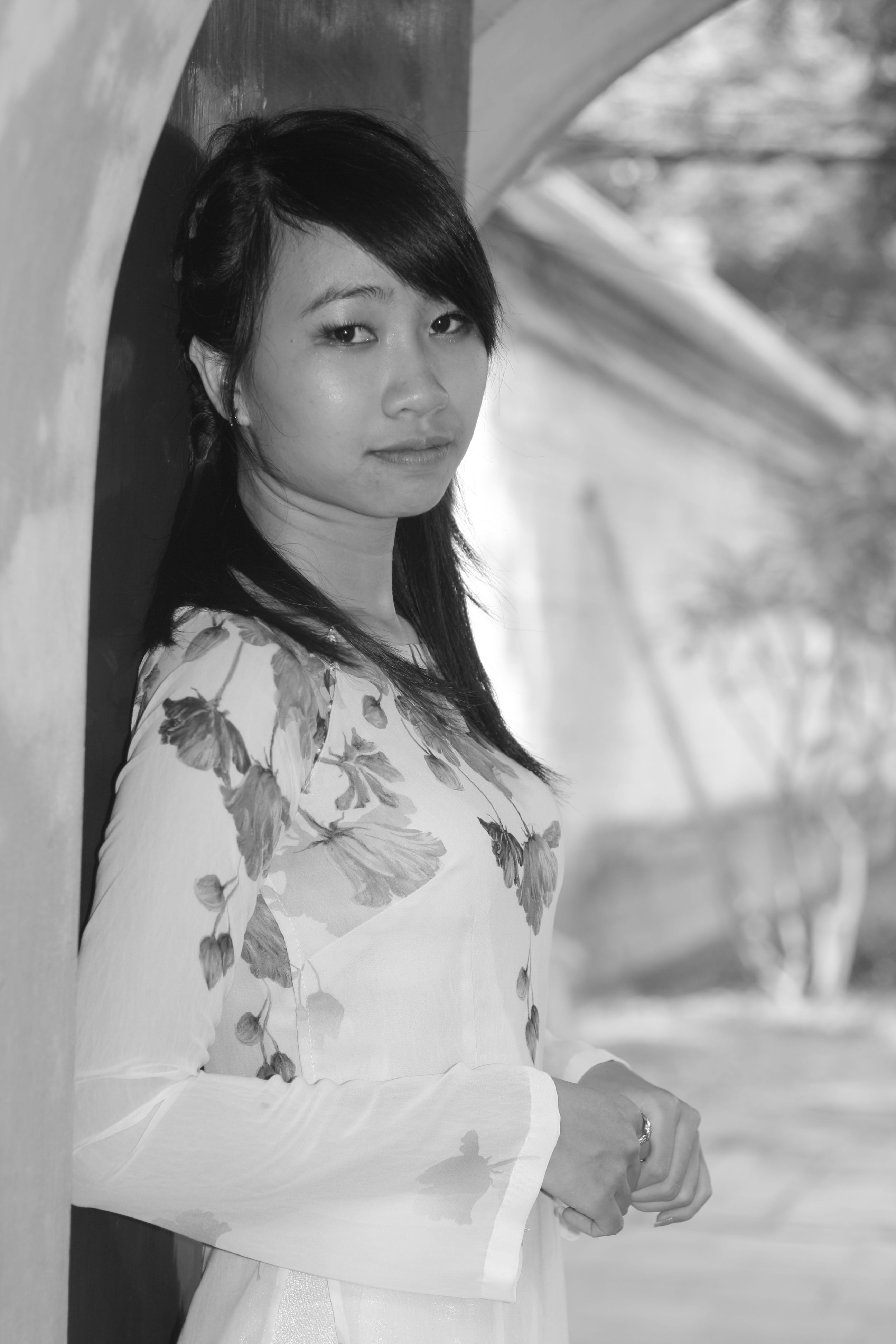 Black and white portrait of a woman in a floral dress, posing outdoors.