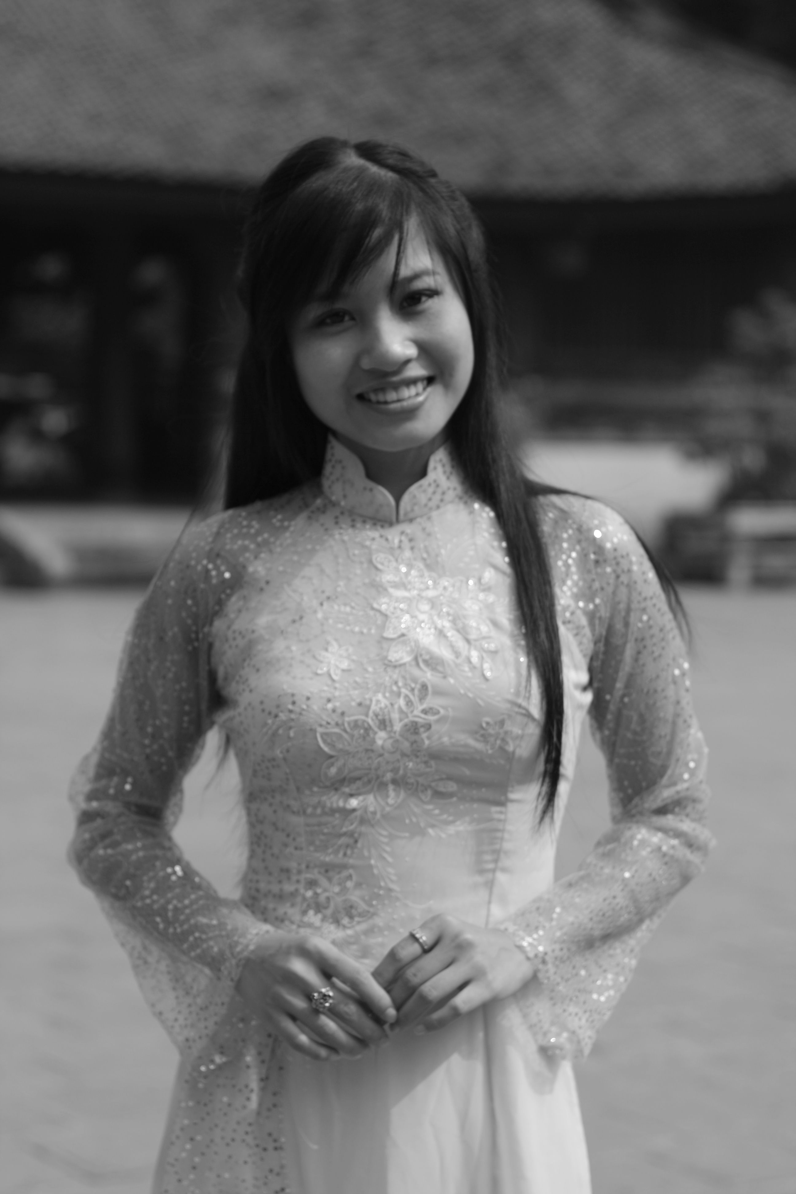 Black and white portrait of a woman smiling in a traditional embroidered Ao Dai.
