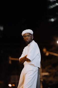 Portrait of a man in stylish white attire under city lights at night.